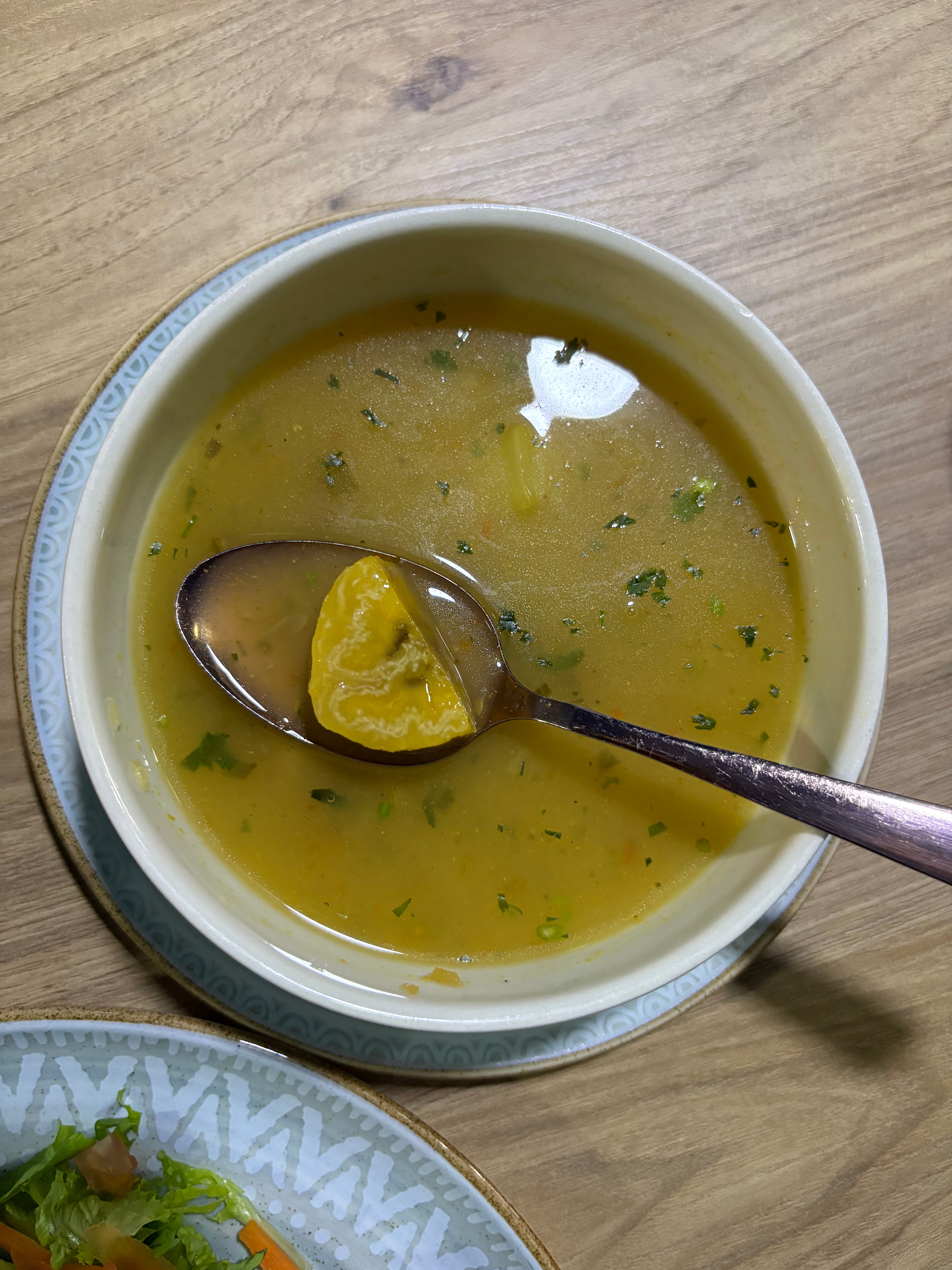 A bowl of golden Afro-Colombian soup with plantain and fresh cilantro, served with a side salad